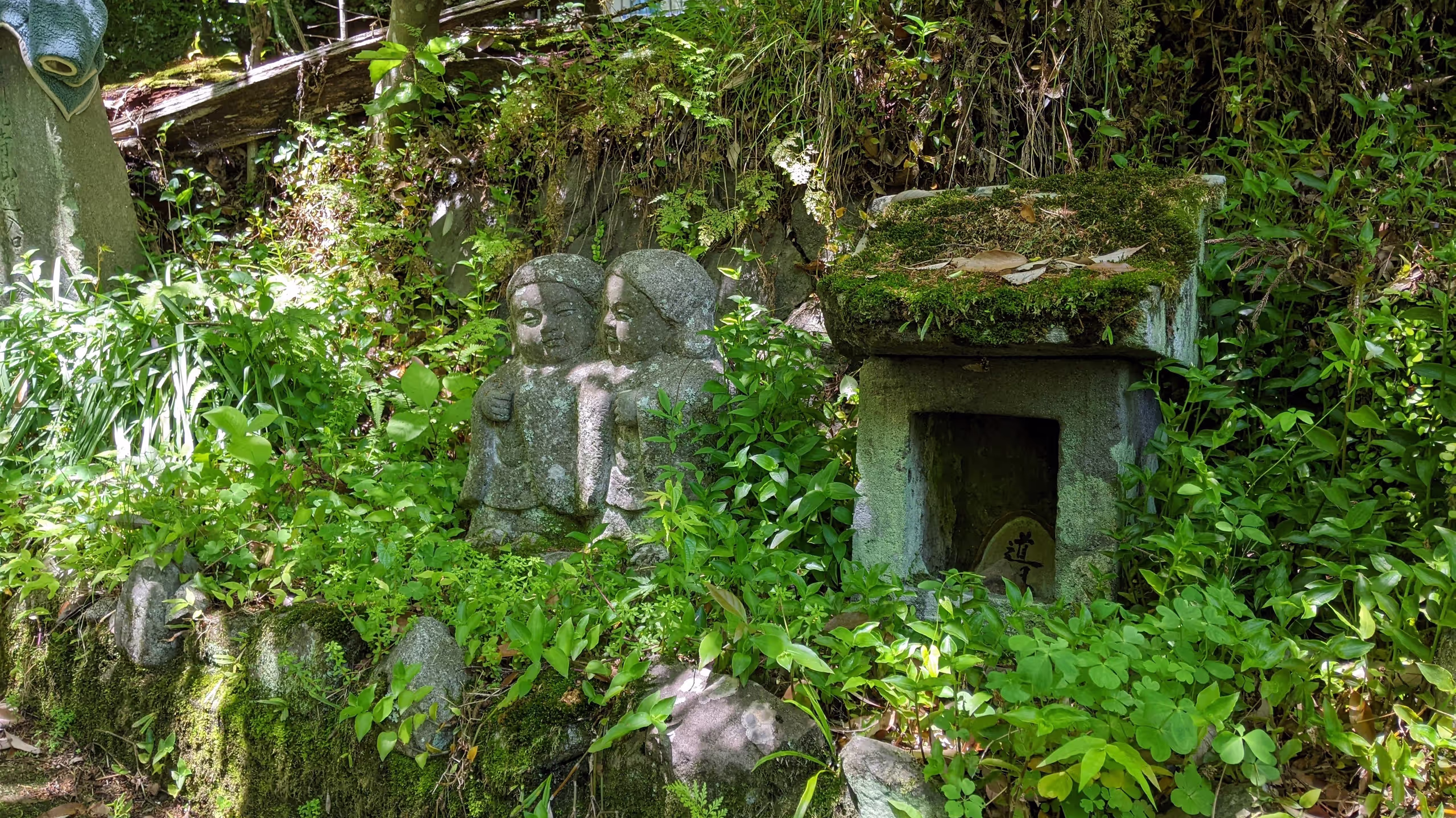 草の生えた斜面に道祖神の祠が埋もれてあり、その横には2体の地蔵が仲良く並んでいる