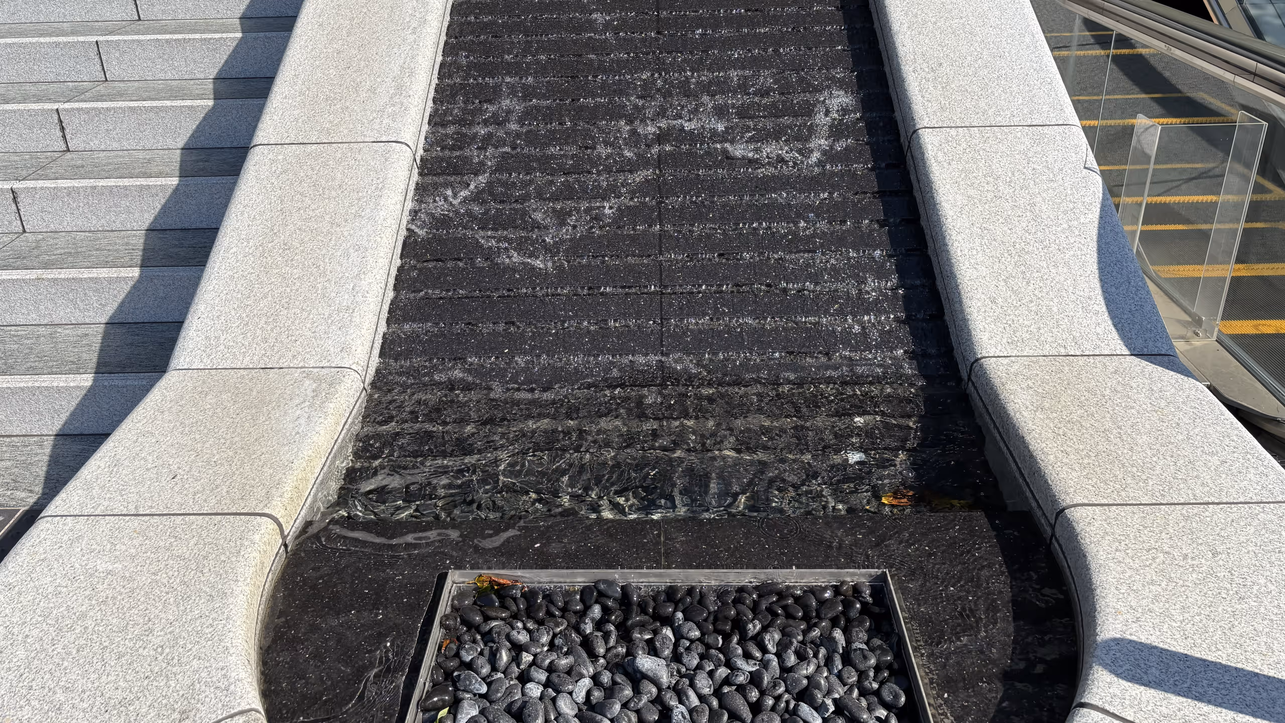 エスカレーターと階段の間に滝のようなものが流れている。滝には階段状の段差が設けられており、波のような模様が流れで出来る仕組みになっているようだ。