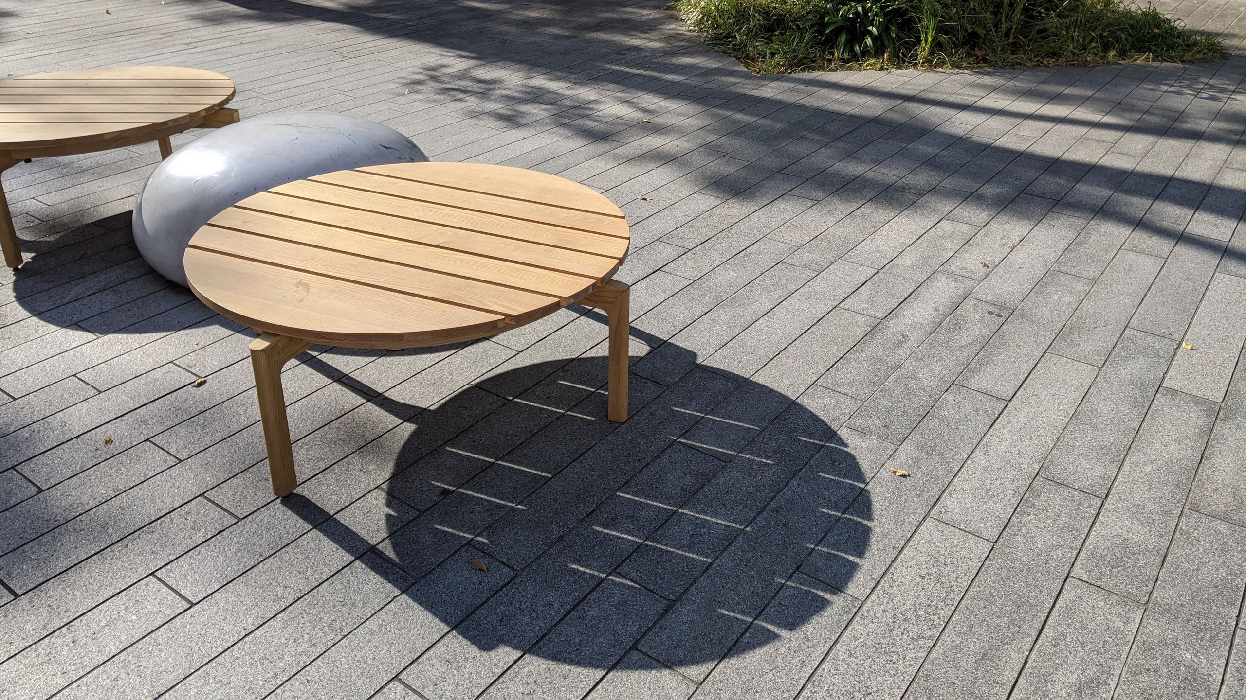 長い木の板を円形になるようつなげ、丸い木の脚がついているテーブル兼ベンチ。